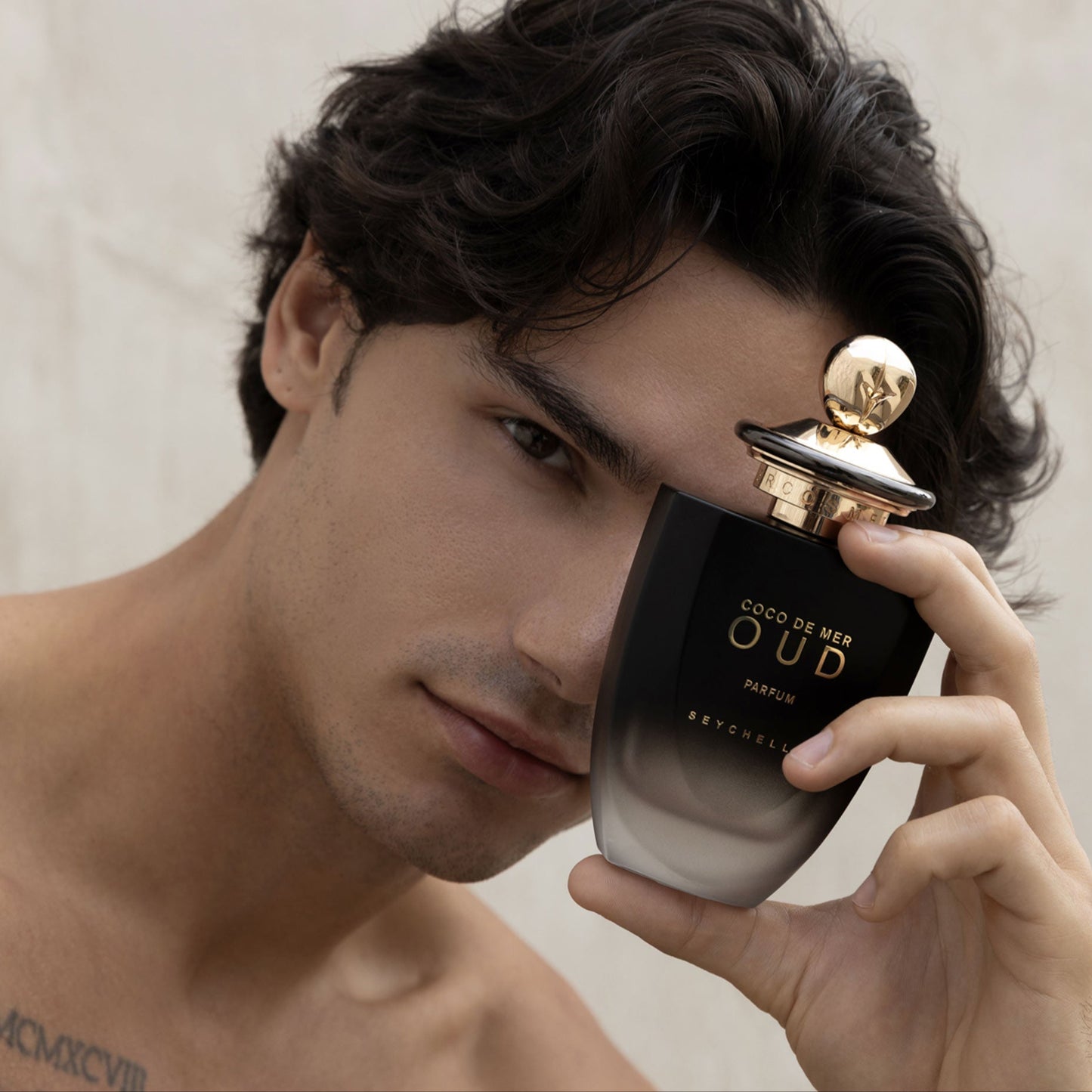 Man holding a black and gold perfume bottle labeled 'Coco de Mer Oud'