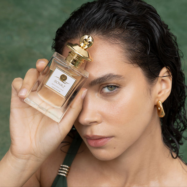 Woman holding a perfume bottle with a gold cap against a green background